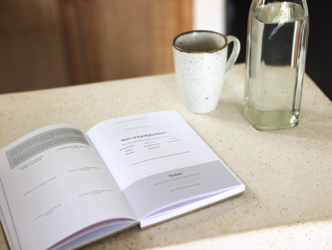 Guidet journaling - Et enkelt værktøj til klarhed og indre ro bog åben på et bord med en kop og vandflaske ved siden af.